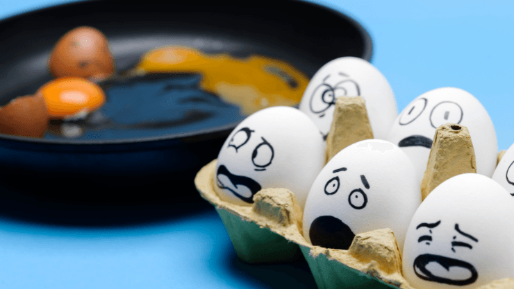 Eggs next to a frying pan. Fearful expressions are drawn on the eggs with permanent marker.