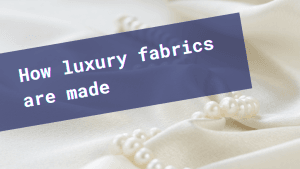 A string of pearls laying atop an elegantly draped white silk and the text: "How luxury fabrics are made."