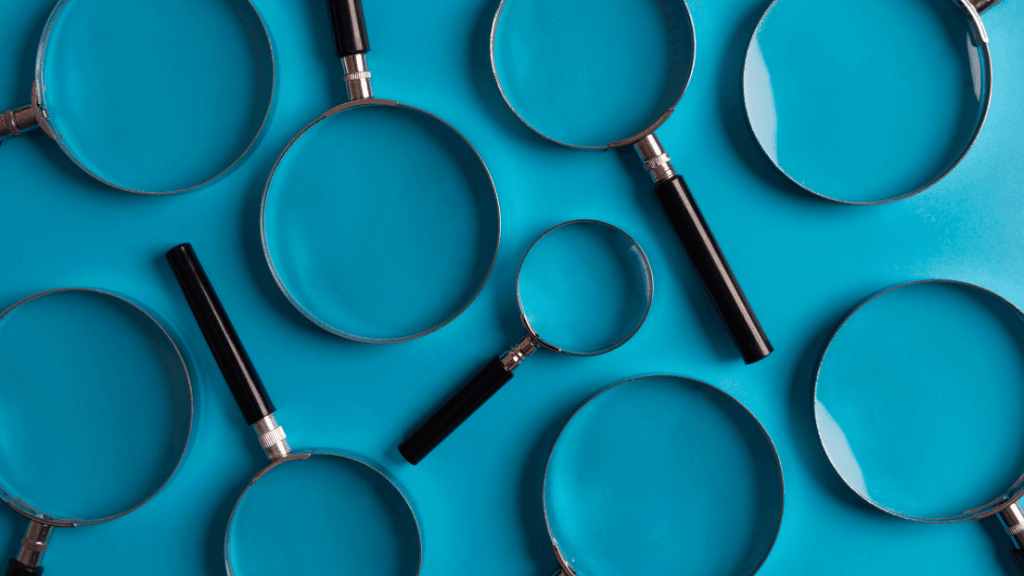 Nine magnifying glasses of different sizes on a teal-colored surface.